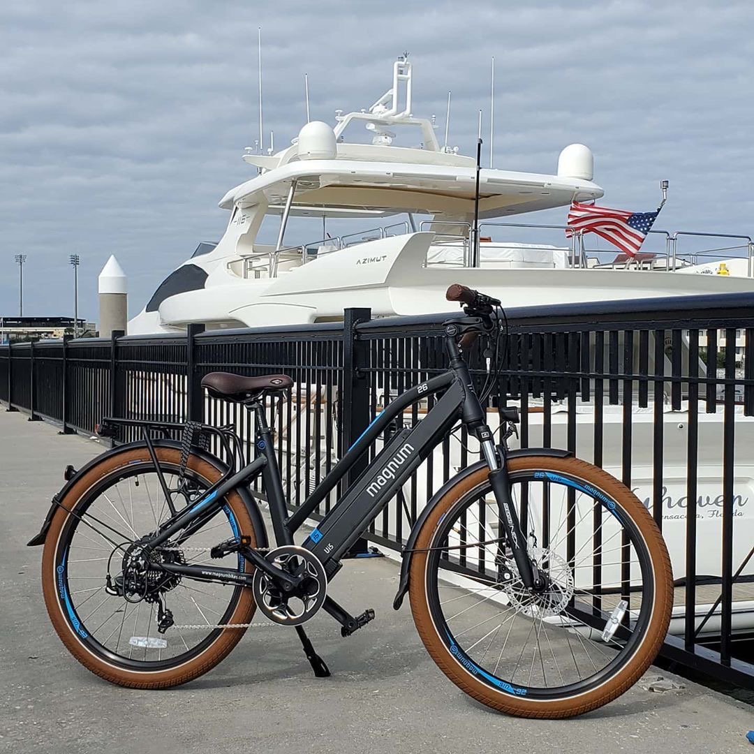 Magnum electric bike parked at the marina with a yacht in the background