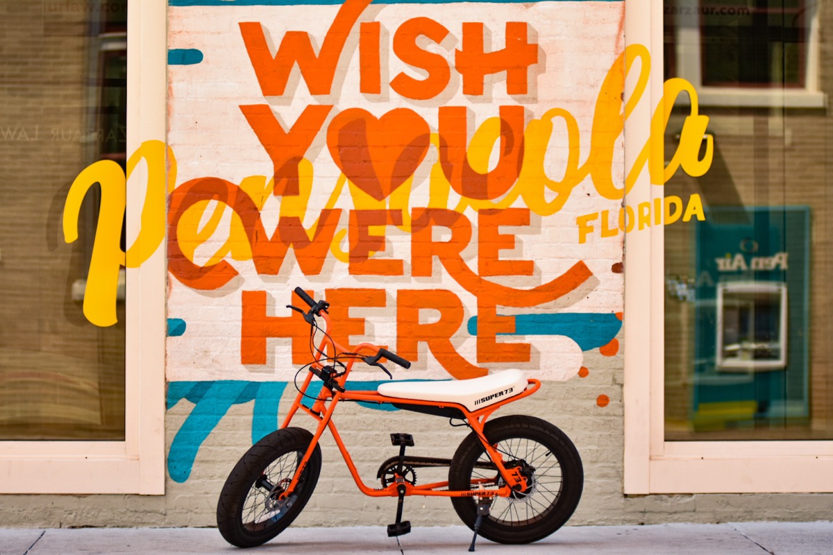 Super73 electric bike in front of a "Wish You Were Here, Pensacola" mural downtown