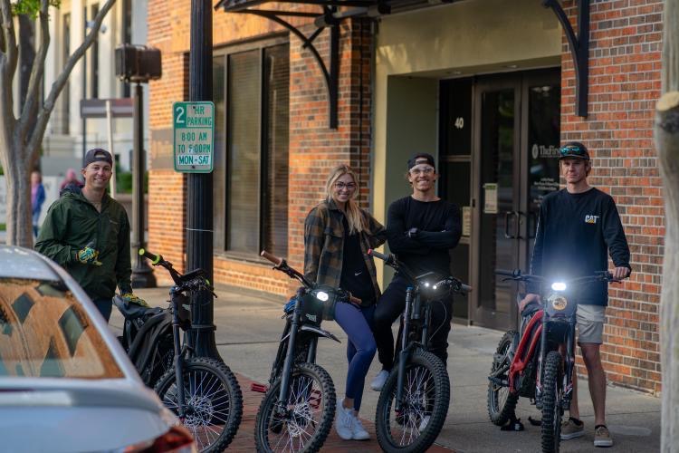 Group of riders posing with their electric bikes on a downtown Pensacola sidewalk