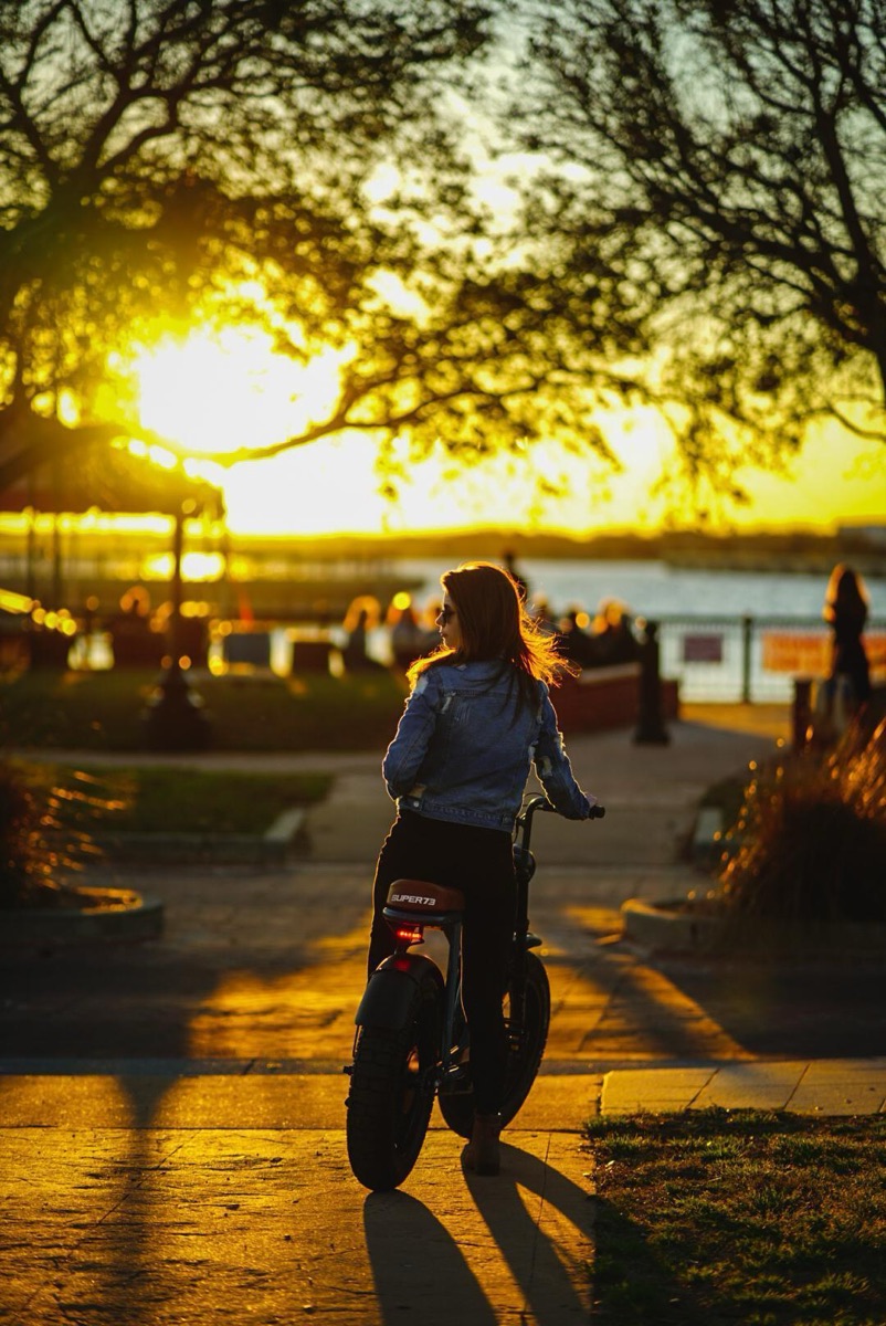 Rider walking a Super73 electric bike along the Pensacola waterfront at sunset