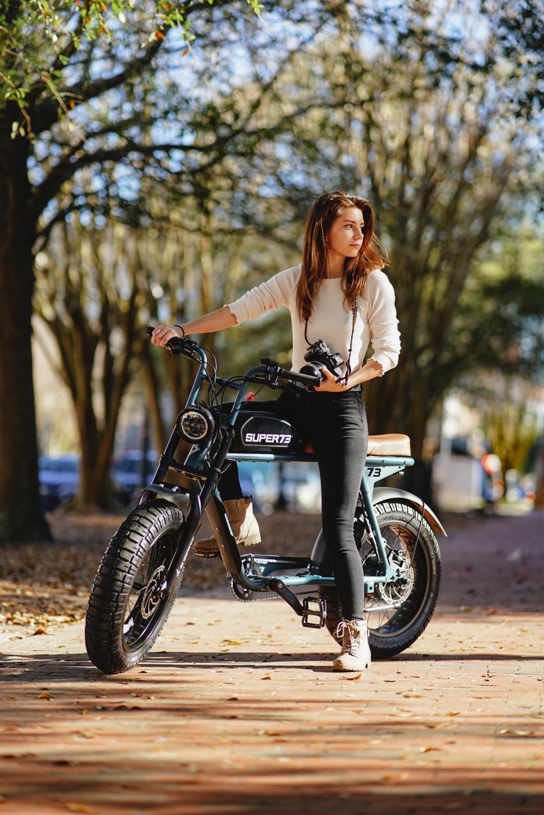 Rider walking a Super73 electric bike along a tree-lined path in downtown Pensacola